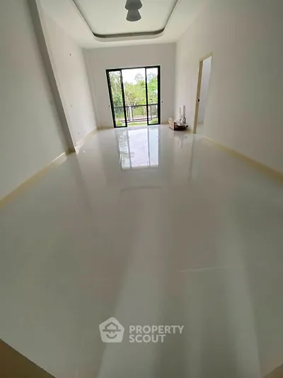 Spacious empty room with glossy floors and large window overlooking greenery.