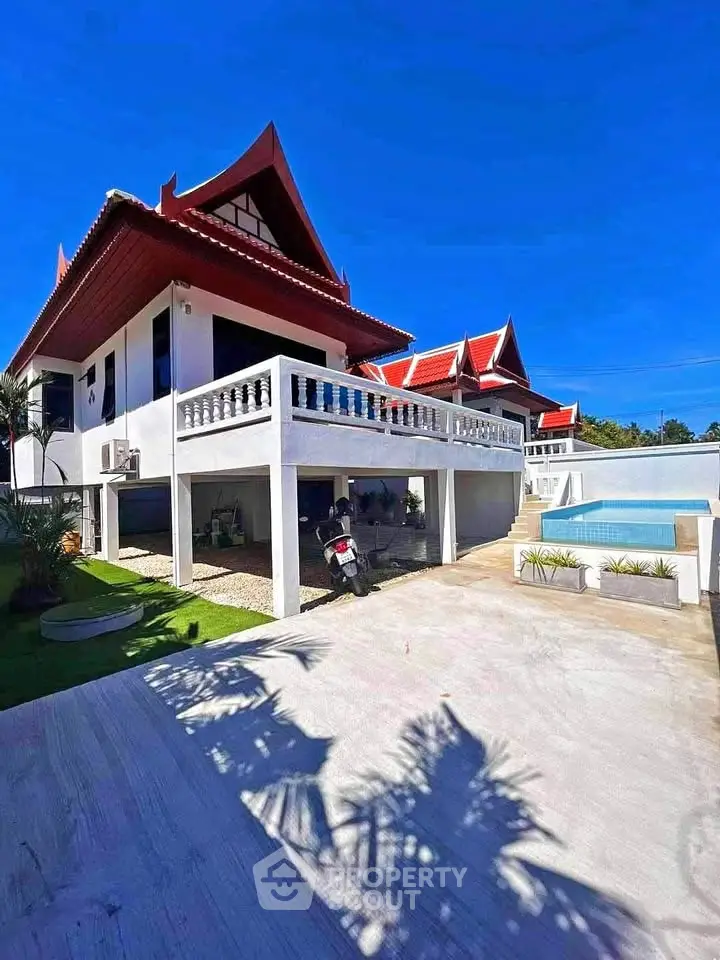 Stunning Thai-style villa with pool and spacious driveway under clear blue skies.