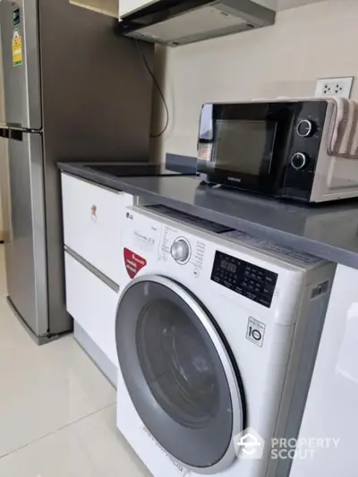 Modern kitchen with washing machine, microwave, and fridge in sleek design.