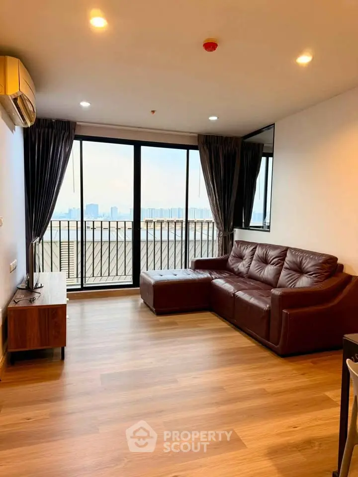 Spacious living room with leather sofa and city view balcony in modern apartment.