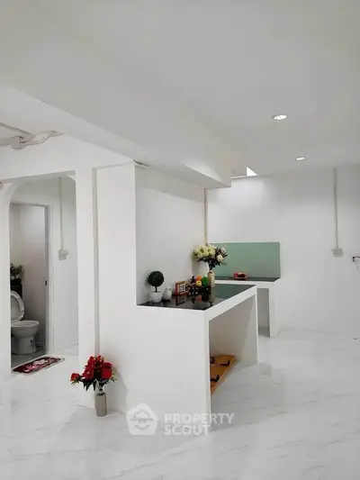Modern minimalist interior with white walls and sleek design, featuring a small kitchen area.