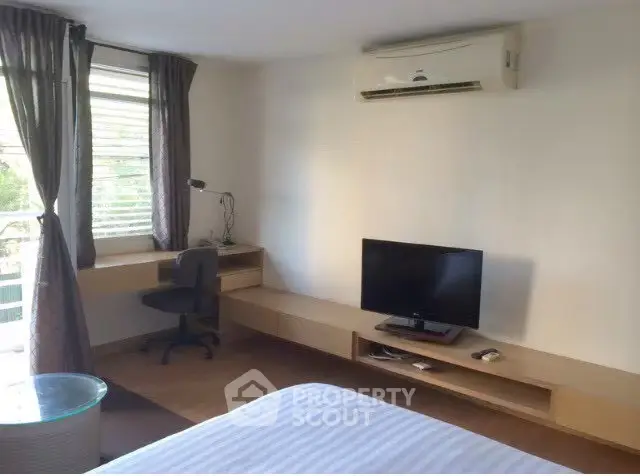Modern bedroom with air conditioning and TV, featuring a sleek desk and large window for natural light.