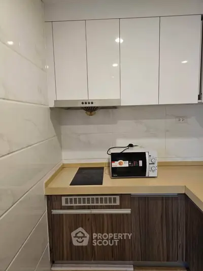 Modern kitchen with sleek cabinetry and built-in appliances, featuring a microwave and electric cooktop.