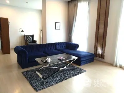 Spacious living room with elegant navy blue sectional sofa, large windows draped in sheer curtains, and a stylish patterned area rug.