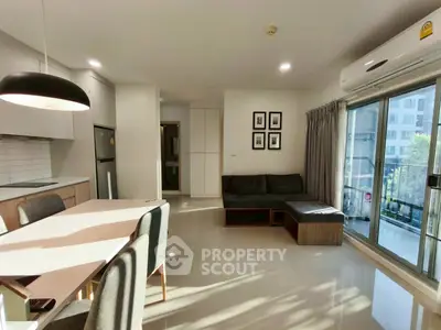 Modern living room with open kitchen and balcony view, featuring sleek furniture and ample natural light.