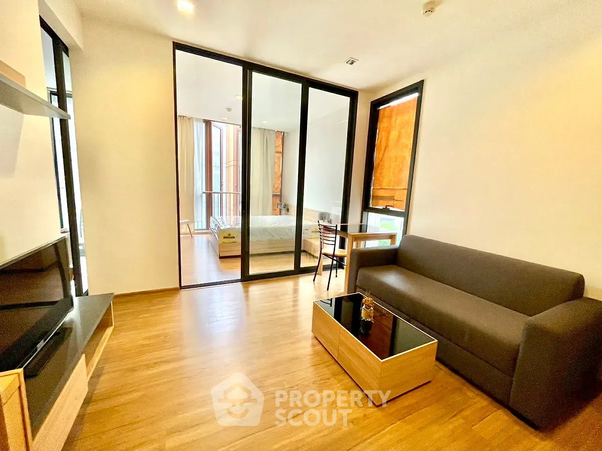 Modern living room with wooden flooring and glass partition leading to bedroom