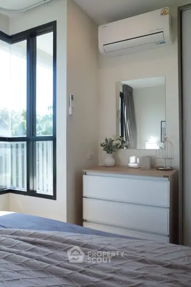 Cozy bedroom with air conditioning and modern decor, featuring a dresser and large windows for natural light.