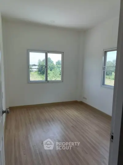 Bright empty bedroom with wooden flooring and large windows offering a serene view.