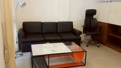 Modern living room with sleek black sofa and ergonomic chair, featuring a stylish glass coffee table.