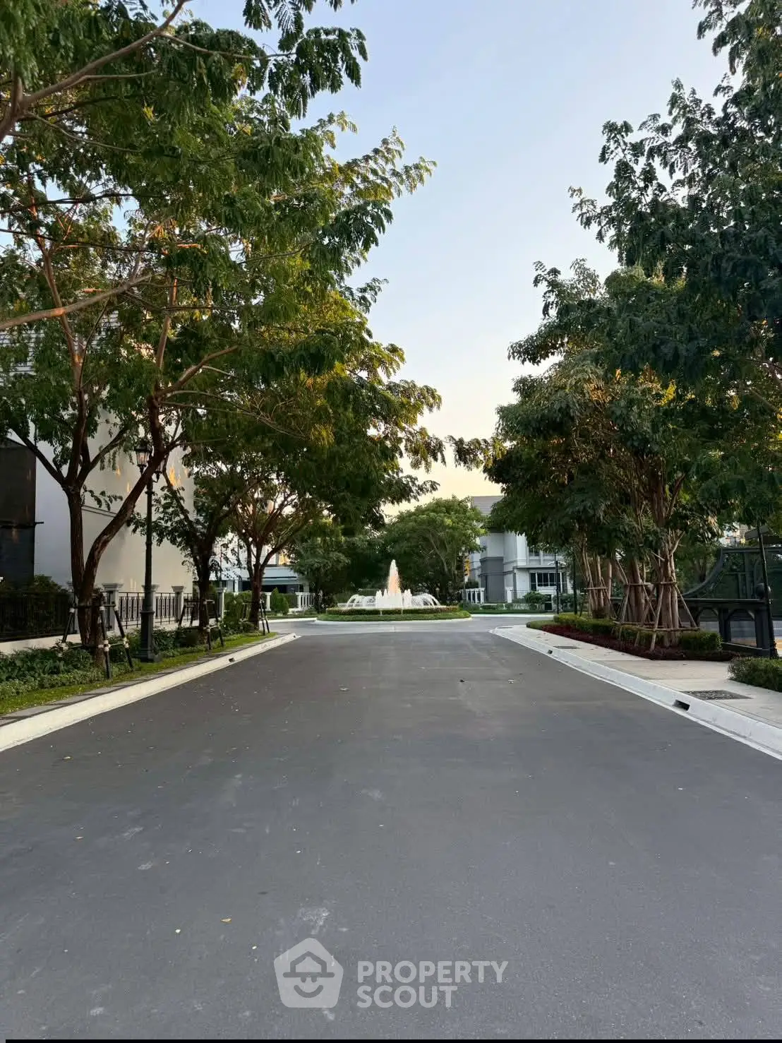 Serene residential street with lush trees and a central fountain, perfect for tranquil living.