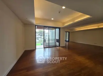 Spacious living room with wooden flooring and large windows offering natural light and outdoor view.