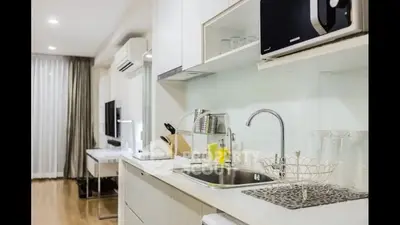 Sleek modern kitchen with white cabinetry and stainless steel sink, complemented by wooden flooring and a cozy living area in the background.