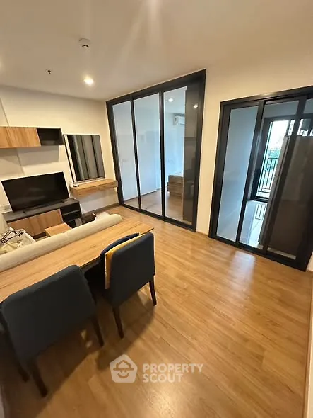 Modern living room with wooden flooring and large glass doors leading to balcony.