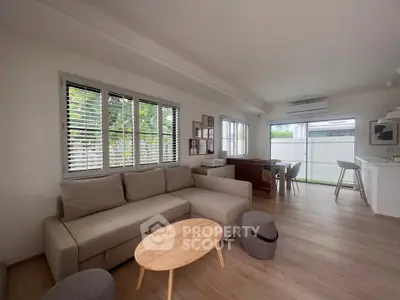 Modern living room with cozy sofa and natural light, open layout to dining area.