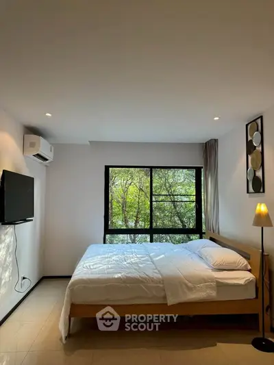 Spacious bedroom with large window and modern decor in a serene setting.