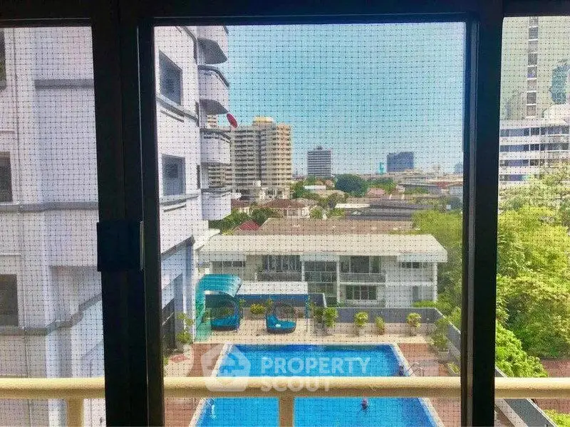 Stunning city view from apartment window overlooking a sparkling pool and urban skyline.