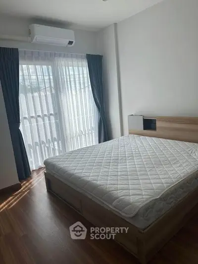 Modern bedroom with wooden flooring and large window, featuring a comfortable bed and air conditioning.