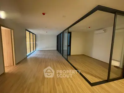 Spacious modern room with wooden flooring and glass partition, ideal for versatile living or office space.