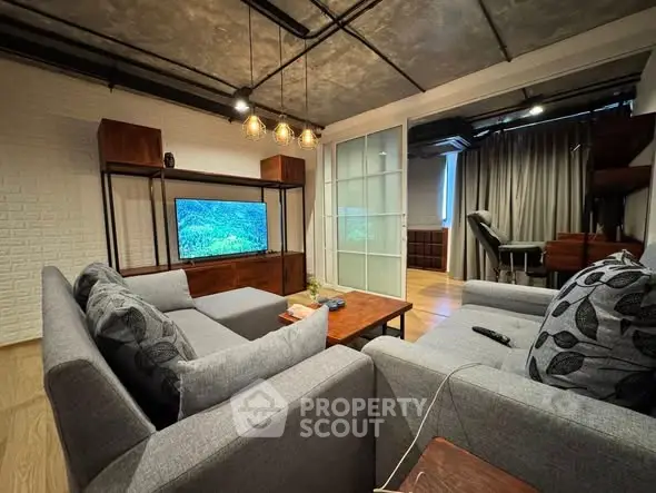 Modern living room with stylish gray sofas and a large TV, featuring industrial ceiling design.