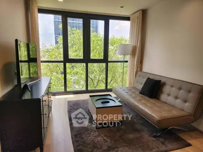 Modern living room with large windows and stylish furniture, offering a serene view of lush greenery.