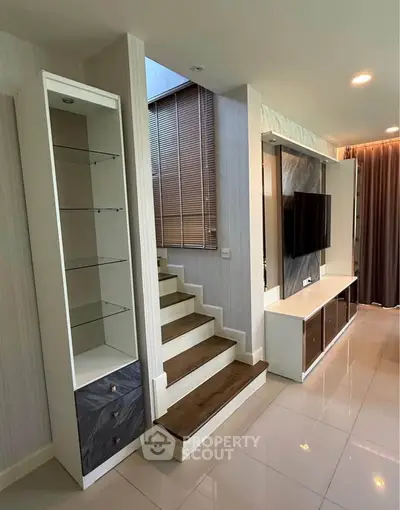 Modern living room with stylish staircase and built-in TV unit, featuring sleek design and ample natural light.
