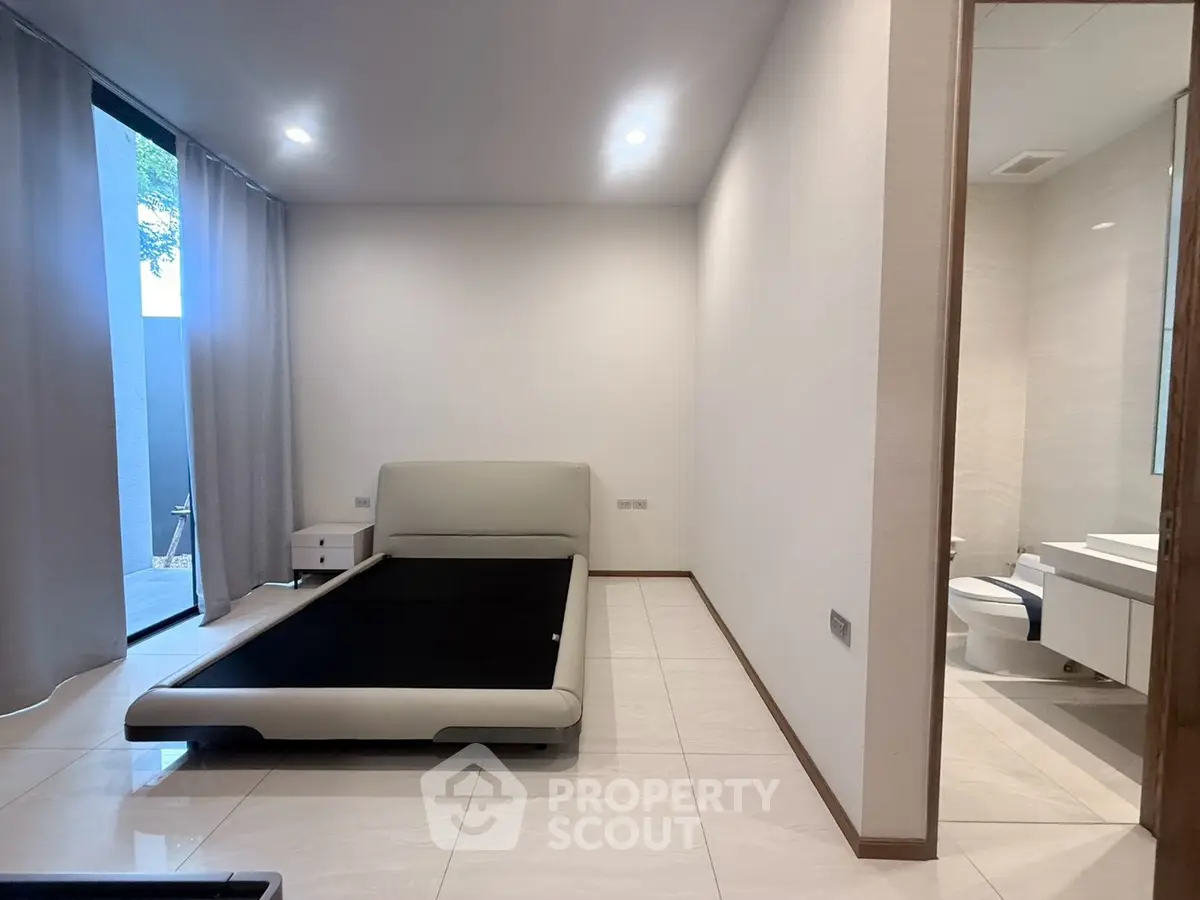 Modern bedroom with sleek design and attached bathroom, featuring minimalist decor and large windows.