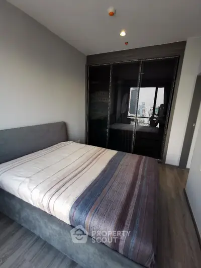Modern bedroom with large window and city view, featuring a sleek bed and stylish wardrobe.