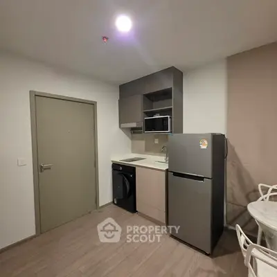 Modern compact kitchen with fridge, microwave, and washing machine in a cozy apartment.