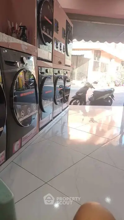 Modern laundry area with multiple washing machines and street view through window.