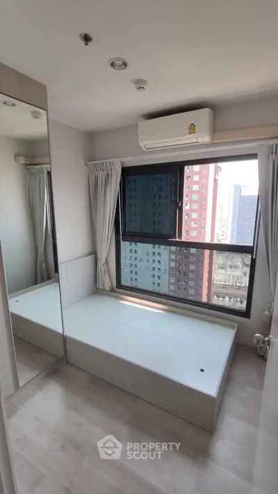 Cozy bedroom with large window and city view, featuring built-in storage and air conditioning.