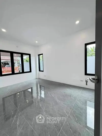 Spacious empty room with glossy marble flooring and large windows in modern home.