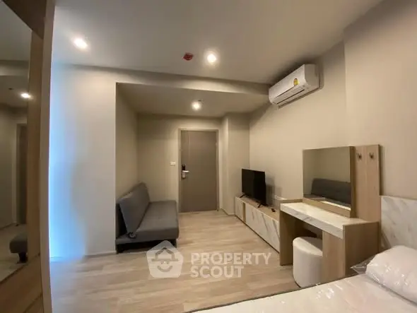 Modern bedroom with minimalist decor, featuring a sofa, TV, and air conditioning unit.