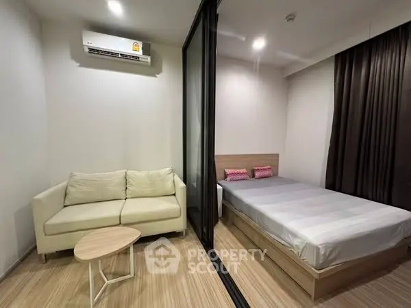 Modern studio apartment with cozy living area and bedroom separated by glass partition.