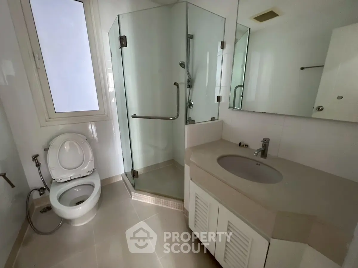 Modern bathroom with glass shower, sleek sink, and toilet in a bright setting.