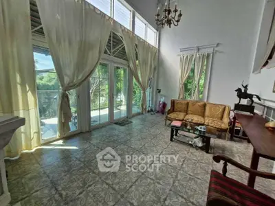 Spacious living room with high ceilings and large windows overlooking greenery, featuring elegant furniture and natural light.