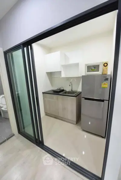 Modern compact kitchen with sleek design and stainless steel fridge in a contemporary apartment.