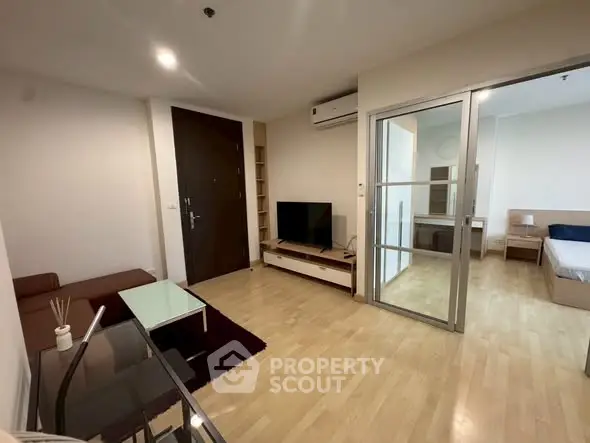 Modern living room with wooden flooring, glass coffee table, and sliding door to bedroom.