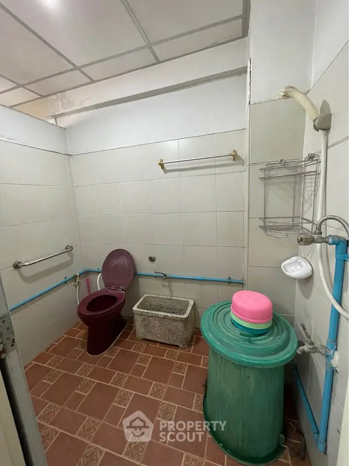 Functional bathroom with unique red toilet and tiled floor, featuring essential fixtures.