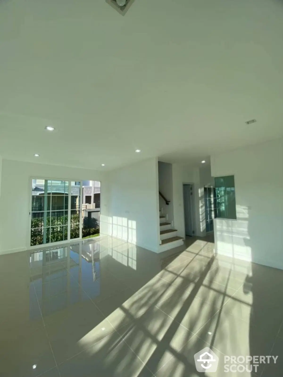 Spacious sunlit living room with glossy tiled floors and modern staircase.