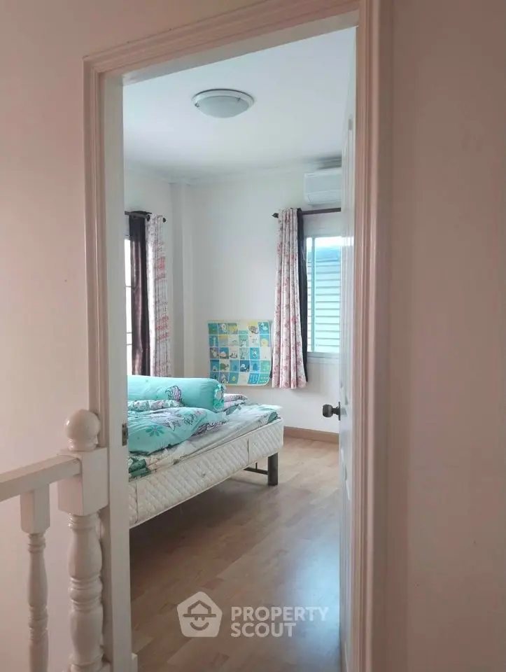 Inviting bedroom with polished hardwood floors, natural light, and charming curtains, perfect for relaxation and comfort in a cozy home setting.