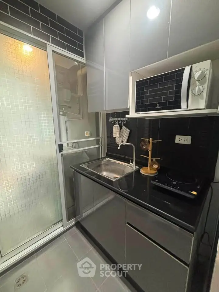 Modern compact kitchen with sleek black countertops and built-in microwave, featuring a glass sliding door.