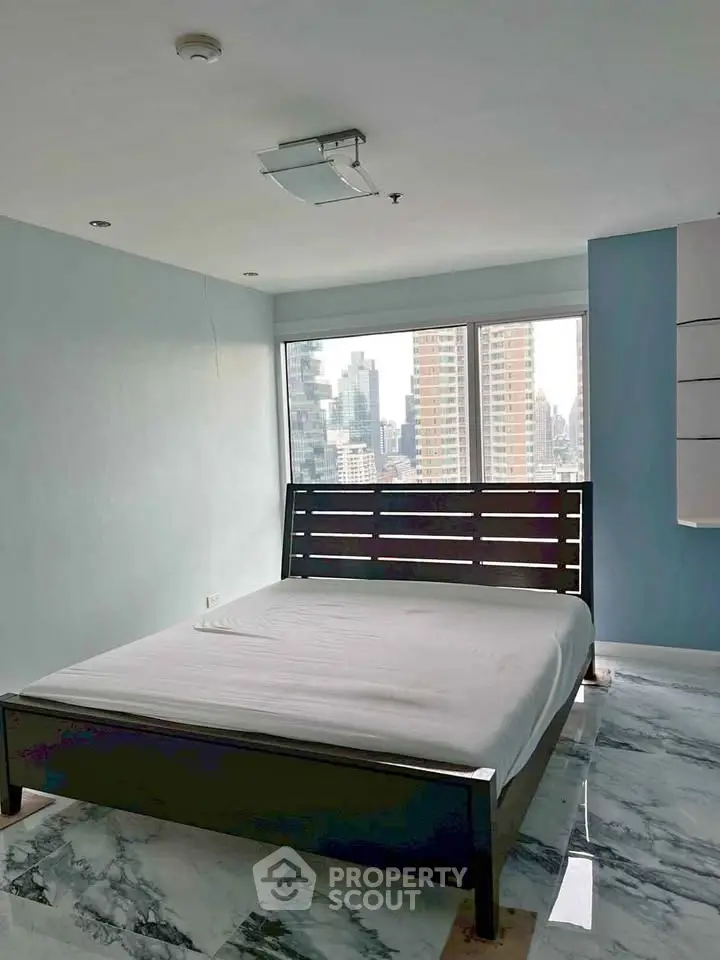 Spacious bedroom with city view and modern decor in high-rise apartment.