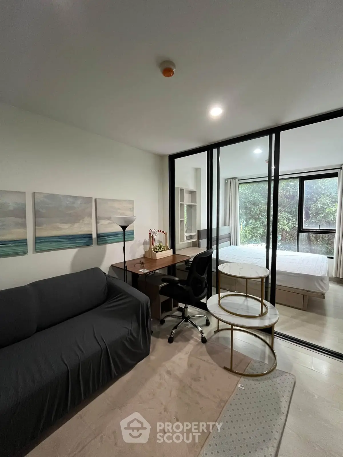 Modern apartment with cozy living area and bedroom separated by glass partition, featuring stylish decor.