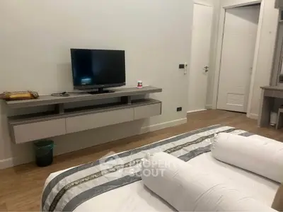 Modern bedroom with sleek TV setup and stylish bedding in a cozy apartment.