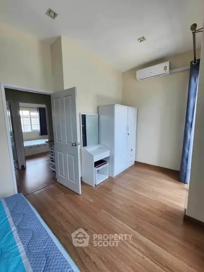 Bright bedroom with wooden flooring and modern furniture, featuring an air conditioner and ample natural light.