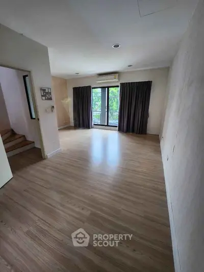 Spacious empty room with wooden flooring and large window overlooking greenery.