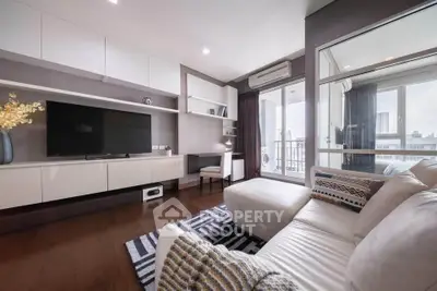 Modern living room with sleek furniture and large TV, featuring a balcony with city views.