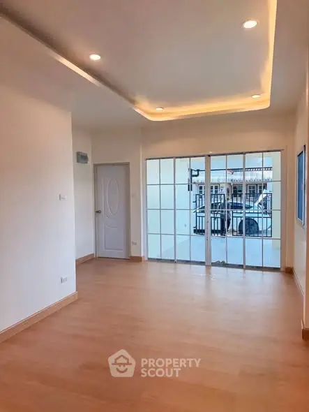 Spacious empty room with wooden flooring and large windows for natural light.