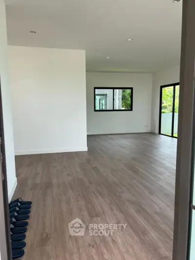 Spacious modern living room with wooden flooring and large windows for natural light.