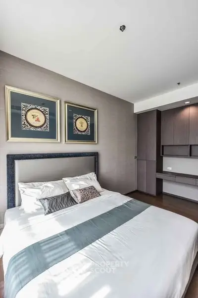 Modern bedroom with stylish decor and ample natural light, featuring elegant artwork and sleek furniture.